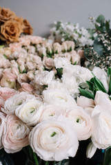 A lot of fresh blossoming flowers (roses, peonies, ranunculus, carnations, eucalyptus) in warm pastel colours at the florist shop