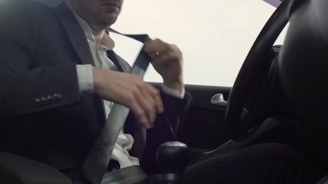 Portrait closeup of caucasian adult man in business suit wearing seat belt for safety, while driving his car on road during afternoon