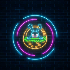 Glowing neon sign of easter bunny in basket in circle frames on dark brick wall background. Easter night greeting banner