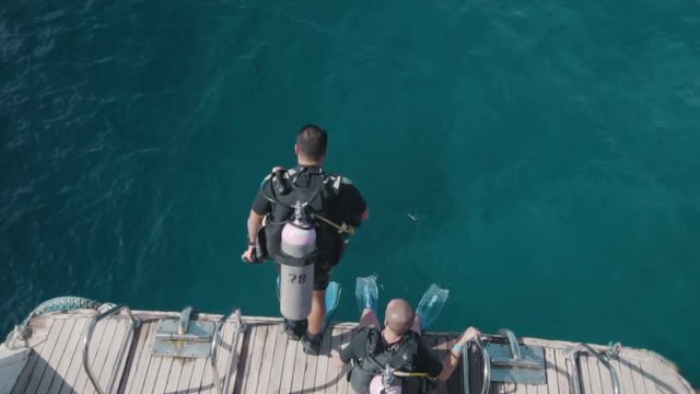 Slow motion Indistinguishable scuba diver jumps into the water from the edge of the boat. View from above.