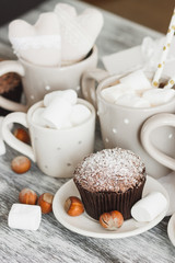 Cups with cacao and marshmallow, cupcakes and different decorations, soft focus background