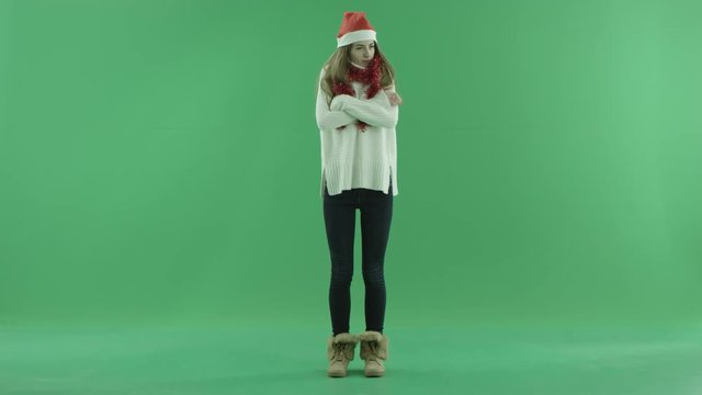 Gorgeous female in Christmas hat freezes and tries to keep herself warm, chroma key on background