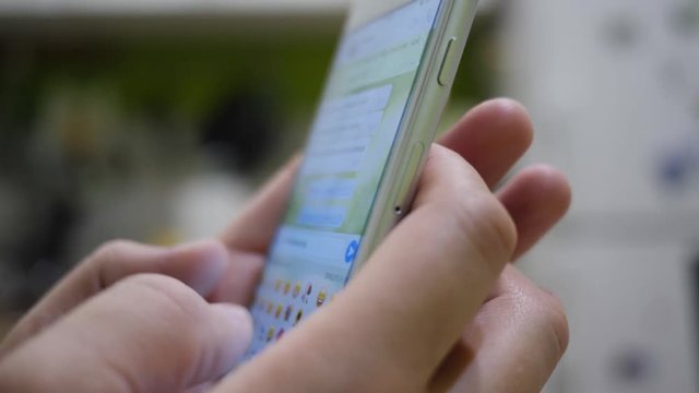 Man types a message and chooses smiley using messanger on a smartphone