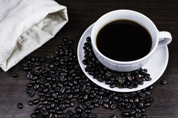 Black coffee in cup and coffee bean and bag on wood background.