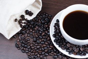 Black coffee in cup and coffee bean and bag on wood background.