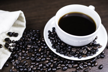 Black coffee in cup and coffee bean and bag on wood background.