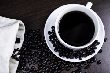 Black coffee in cup and coffee bean on wood background.