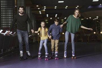 happy family holding hands while skating together on roller rink