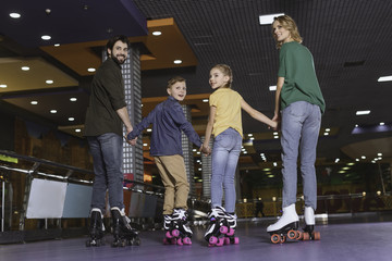 back view of family holding hands while skating on roller rink together