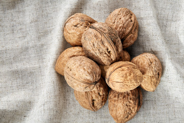A stack of hard shells of walnuts piled together on light grey fabric cotton tablecloth, selective focus