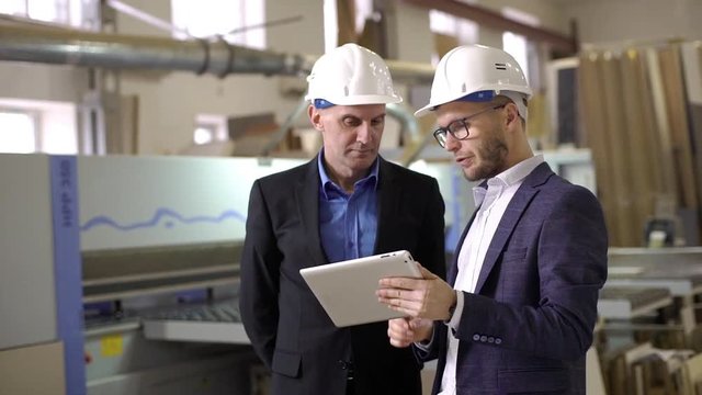 Two adult male executive manager and director discussing process of work on furniture manufacture, while watching in digital tablet slow motion