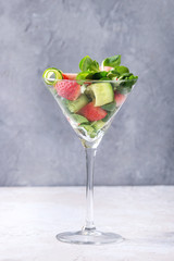 Spring summer diet salad with strawberries, cucumber, green field salad and yogurt mint sauce served in cocktail glass over grey texture background. Copy space