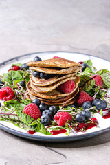 Vegan chickpea pancakes served in plate with green salad young beetroot leaves, sprouts, berries, berry sauce over grey kitchen table. Close up. Healthy eating