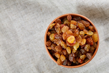 Ceramic bowl with golden raisins on light tablecloth, close-up, selective focus