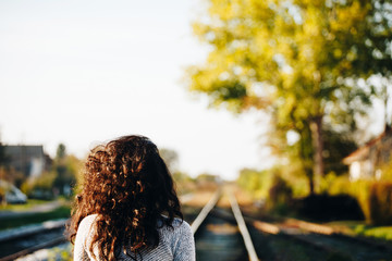 Beautiful woman/girl with a nice curve hair walking on rails, back to a camera, on nature, in the summer
