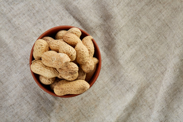 Unpeeled peanuts in ceramic bowl closeup, selective focus