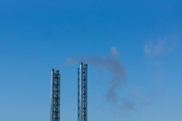 Factory pipes with smoke on blue sky background