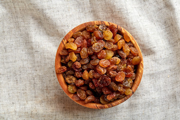 Wooden bowl with golden raisins on light tablecloth, close-up, selective focus