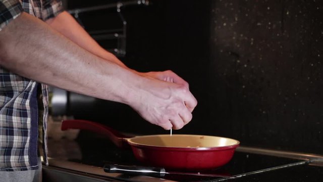 breaks an egg with a knife above a frying pan for cooking scrambled eggs