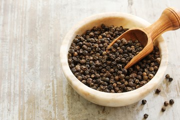 Whole Black Pepper in a bowl with wooden scoop, selective focus