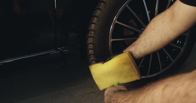 A professional specialist holds a yellow sponge and spray, a black car.