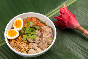 Spicy noodle soup with pork and egg in bowl on banana leaf