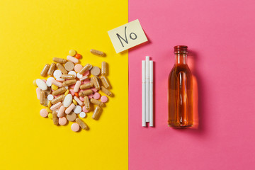 Medication colorful tablets pills arranged abstract, bottle alcohol, cigarettes on yellow pink rose...