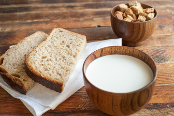 Two bread slices on a white napkin, a cup of milk and crackers on an old wooden table.