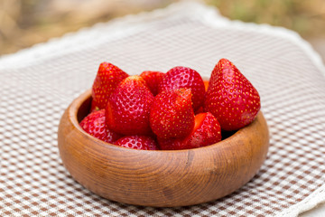 The fresh strawberries in the woonden bowl on the mat. 