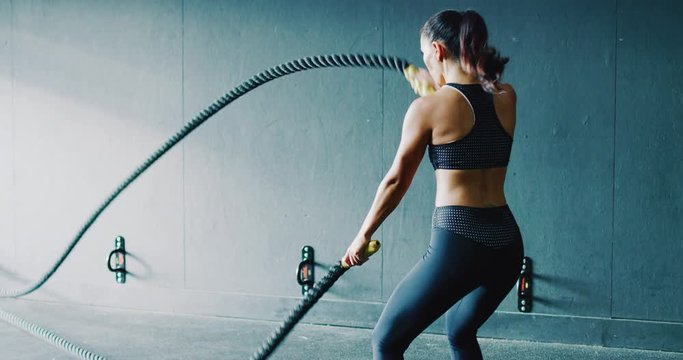 Beautiful athletic woman exercising with battle ropes in the gym