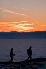 Naklejka na ściany i meble Two hikers walking on mountain over low stratus to sunset
