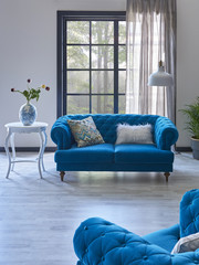 modern wall and windows living room corner decor blue sofa and armchair. white coffee table and vase of plant decor.