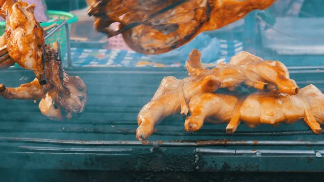 Whole chicken carcass grill strung on wooden stick grilling on the grill. Street Food Thailand. Men's hands turn over the grilled chicken