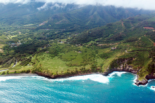 Aerial view of Maui's coastline shows everything from Pacific surf to green fields to mountains and clouds, shot from a small, low-flying prop plane