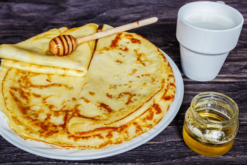 Pancakes on a white plate with honey and a cup of milk. Wooden background in a rustic table.