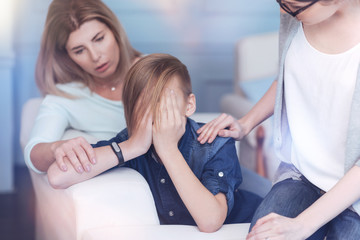 Fototapeta premium Anxiety and depression. Worried mother and professional psychotherapist trying to calm a teenage boy down while hovering his face and crying.