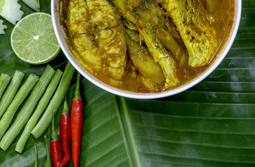 Yellow curry snapper fish with Lotus Stems, Southern Thai Spicy food and fresh vegetable in white dish on banana leaf / selective focus