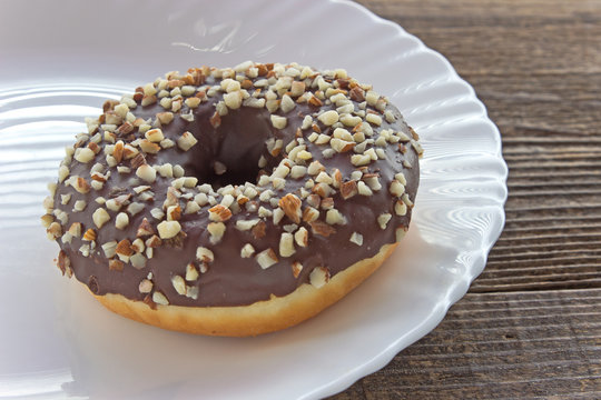 Donut with chocolate and chopped almonds in plate on table