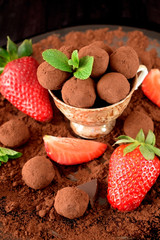 Chocolate truffles covered with cacao powder in a brown cup surrounded by strawberries