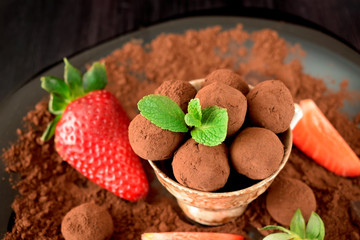 Chocolate truffles covered with cacao powder in a brown cup surrounded by strawberries