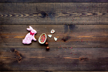 Easter composition. Easter sweet gift. Chocolate eggs near cookies in shape of Easter bunny on dark wooden background top view space for text