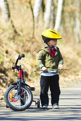 Little boy on bicycle in green park outdoor in summer. A child is riding a children's bike with support wheels  wearing safety helmet