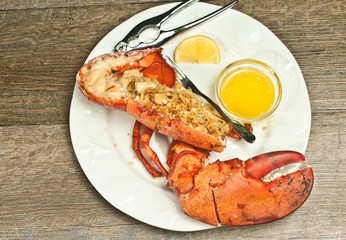Top view, half, roasted lobster, stuffed, bread crumbs, sliced scallops, on round, white plate,  nut cracker and artisan fork slice of lemon and glass bowl of melted butter