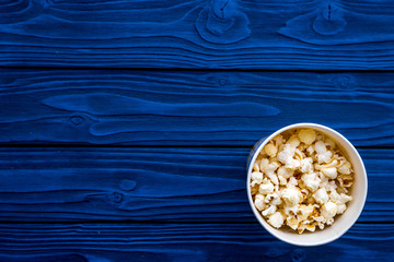 Snacks for film watching. Popcorn in paper cup on blue background top view copy space