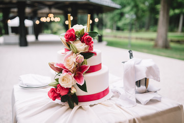 Beautiful wedding cake decorated with flowers and ribbons on white table