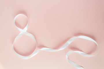 White gift celebration ribbon in 8 digit shape over pink background