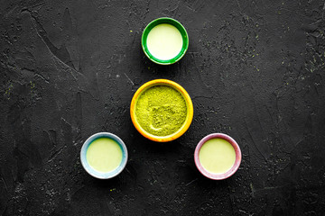 Brew matcha tea. Bowl with powder and cups with beverage on black background top view copy space
