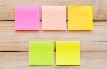 five blank sticky note or post note colorful yellow green and pink on wood table or wood board.