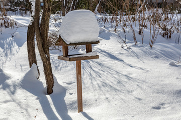 Wooden bird feeder in the snow-covered winter city park
