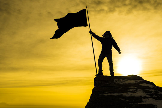 silhouette of man on top of mountain with victory flag, background sky with rays of sunset sunset. Business concept idea